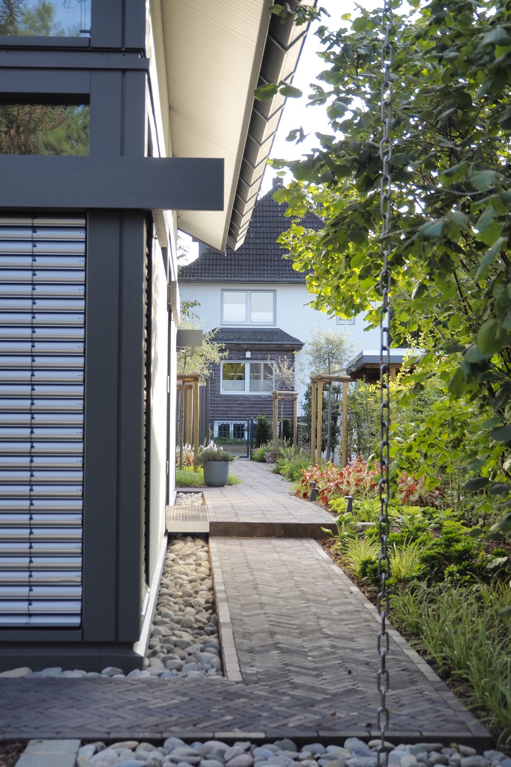 Der hintere Gartenbereich bietet schattigen Rückzug und die erhaltenden Haselsträucher stellen Sichtschutz her.